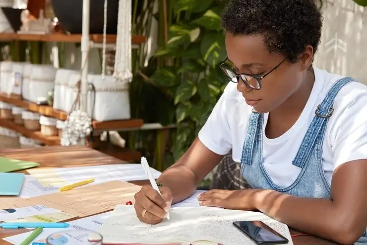 Female students writing down some work in her notebook - Campus Weekly